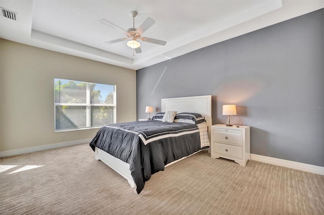 bedroom with ceiling fan, a raised ceiling, and light carpet