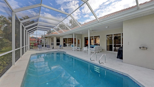 view of swimming pool with glass enclosure, ceiling fan, and a patio