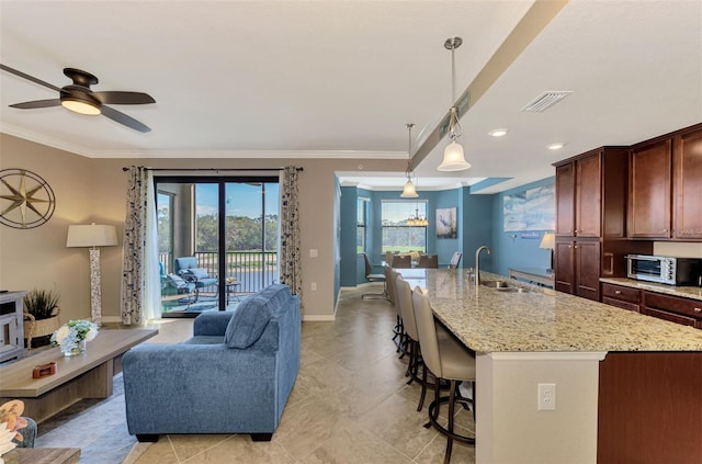 kitchen featuring ceiling fan, sink, hanging light fixtures, an island with sink, and ornamental molding