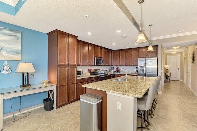 kitchen featuring light stone counters, stainless steel appliances, sink, a center island with sink, and hanging light fixtures