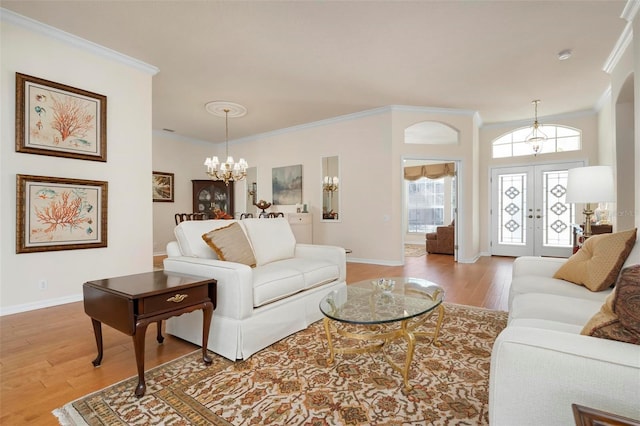 living room with a notable chandelier, wood-type flooring, crown molding, and french doors