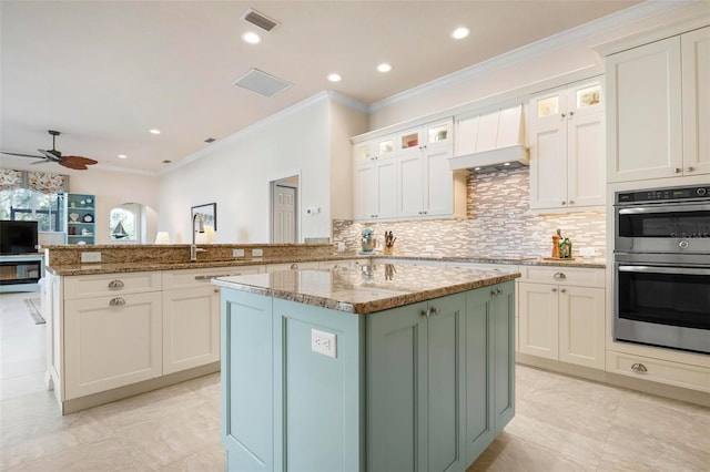 kitchen featuring sink, stainless steel double oven, light stone counters, kitchen peninsula, and a kitchen island