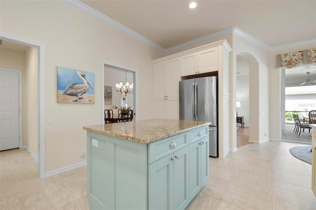 kitchen featuring stainless steel refrigerator, white cabinetry, light stone counters, a kitchen island, and ornamental molding