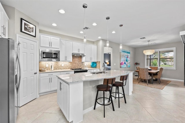 kitchen featuring a center island with sink, sink, hanging light fixtures, appliances with stainless steel finishes, and white cabinetry