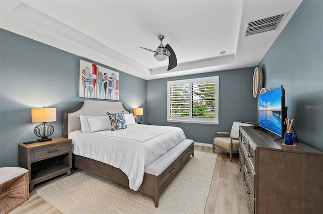 bedroom with ceiling fan, light hardwood / wood-style floors, and a tray ceiling