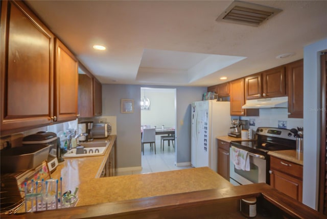 kitchen featuring kitchen peninsula, white appliances, a tray ceiling, sink, and light tile patterned floors