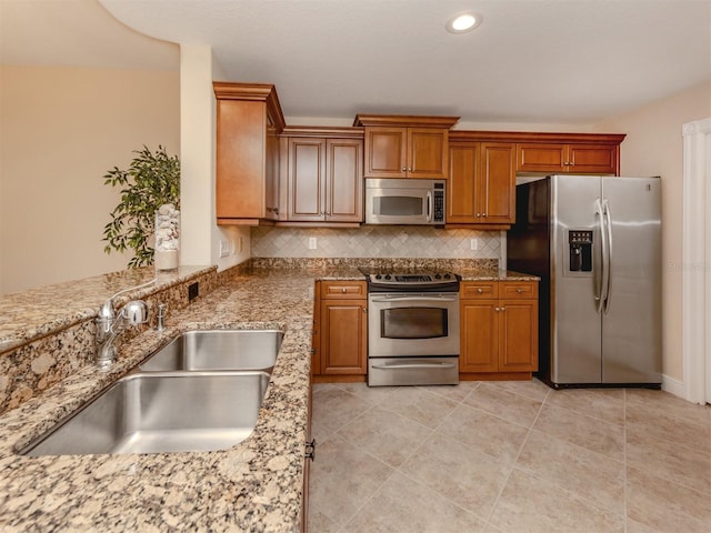 kitchen featuring decorative backsplash, stainless steel appliances, light stone counters, and sink