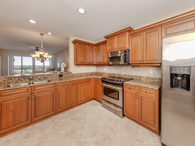 kitchen with decorative backsplash, appliances with stainless steel finishes, light stone counters, sink, and hanging light fixtures