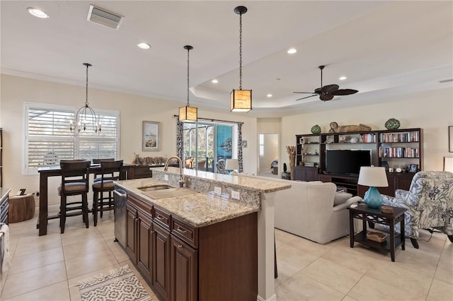 kitchen with a kitchen island with sink, a raised ceiling, sink, light stone countertops, and decorative light fixtures