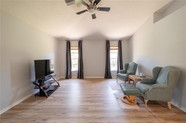 living area with ceiling fan, a textured ceiling, and light wood-type flooring