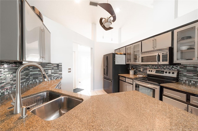 kitchen featuring decorative backsplash, stainless steel appliances, ceiling fan, sink, and dark stone countertops