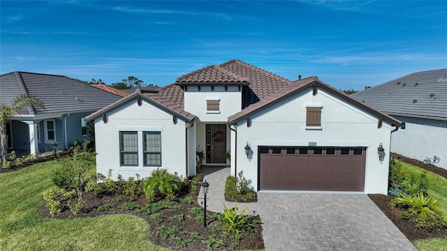 mediterranean / spanish-style home with decorative driveway, stucco siding, an attached garage, a tiled roof, and a front lawn