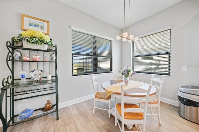 dining area featuring light wood-type flooring, a notable chandelier, and baseboards