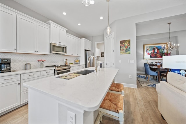 kitchen featuring a kitchen island with sink, stainless steel appliances, white cabinets, and pendant lighting