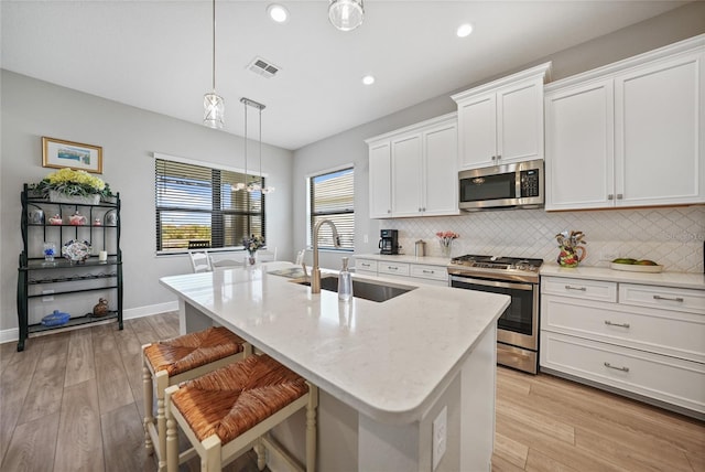 kitchen with stainless steel appliances, a sink, visible vents, white cabinetry, and an island with sink