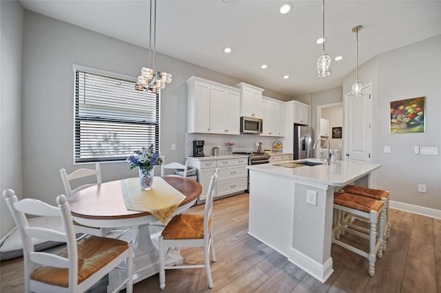 kitchen with stainless steel appliances, an island with sink, light countertops, and decorative light fixtures