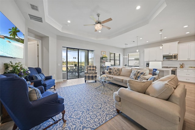 living room featuring light wood finished floors, a tray ceiling, and visible vents