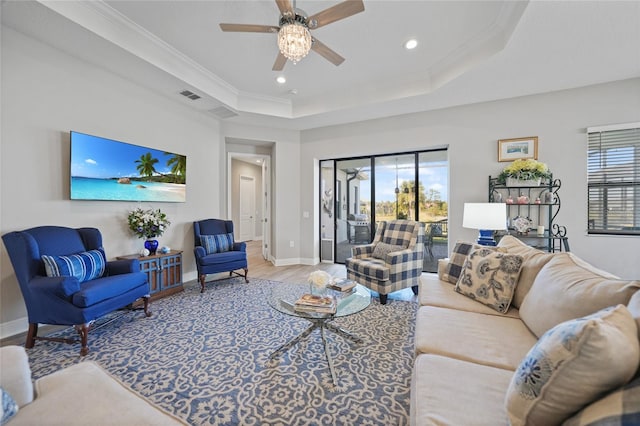 living area featuring baseboards, visible vents, wood finished floors, a tray ceiling, and crown molding