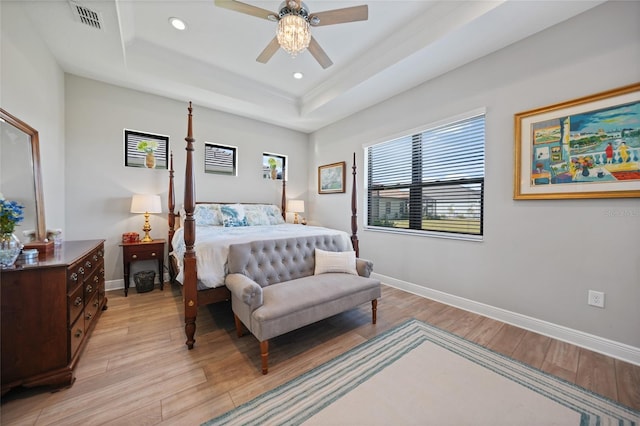 bedroom featuring a raised ceiling, visible vents, baseboards, and light wood finished floors