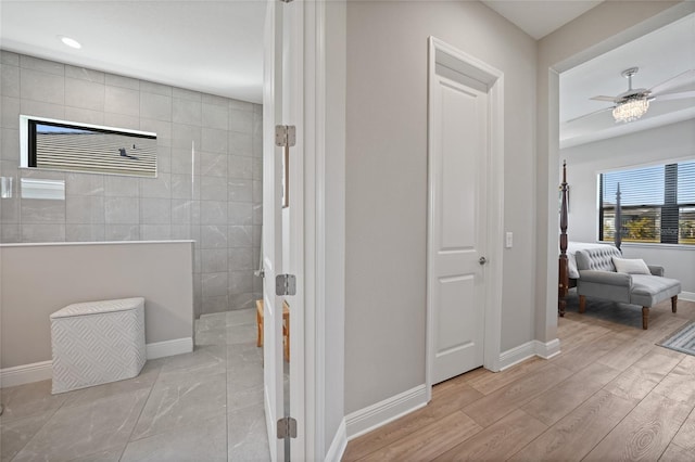 bathroom featuring tile walls, a ceiling fan, wood finished floors, baseboards, and a walk in shower