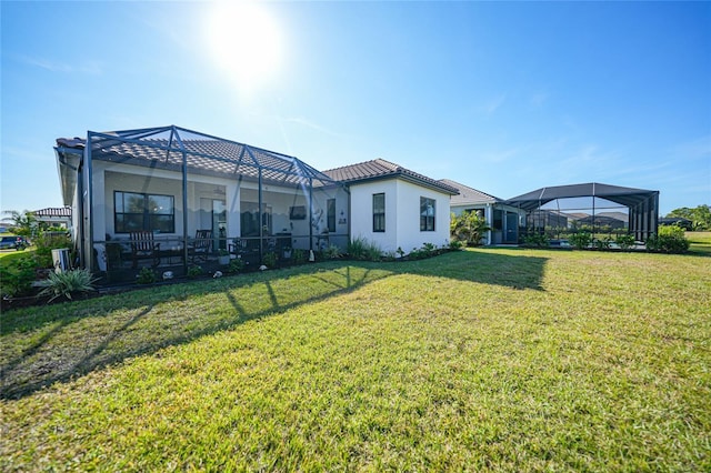 rear view of house featuring glass enclosure, a tile roof, stucco siding, and a yard