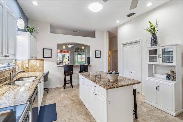 kitchen featuring sink, white cabinetry, a center island, hanging light fixtures, and light stone countertops