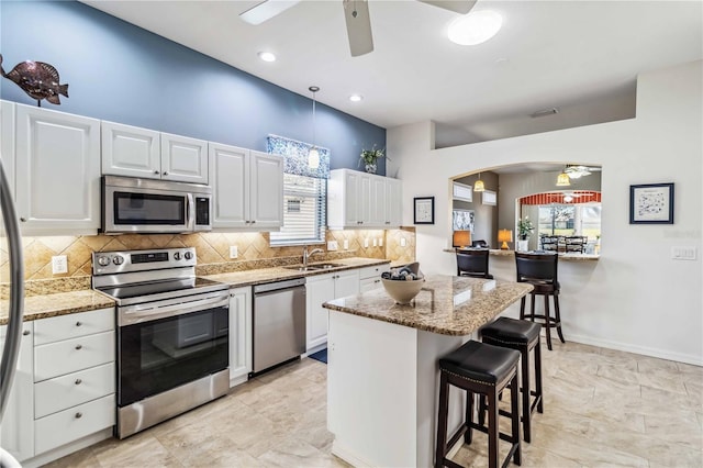 kitchen featuring white cabinetry, appliances with stainless steel finishes, a kitchen breakfast bar, and hanging light fixtures