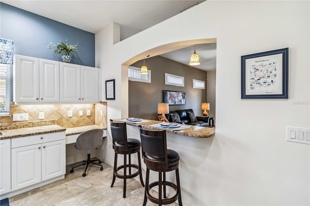 kitchen featuring a breakfast bar, tasteful backsplash, hanging light fixtures, light stone countertops, and white cabinets