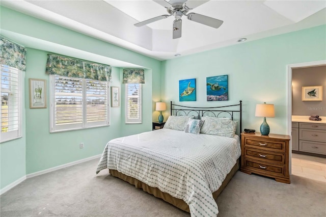 bedroom featuring ensuite bathroom, light carpet, ceiling fan, and a tray ceiling