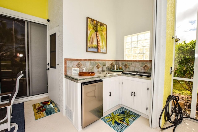 kitchen with sink, decorative backsplash, stainless steel refrigerator, and white cabinets