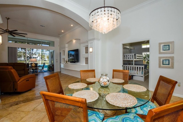 tiled dining area featuring ceiling fan with notable chandelier, ornamental molding, and a high ceiling