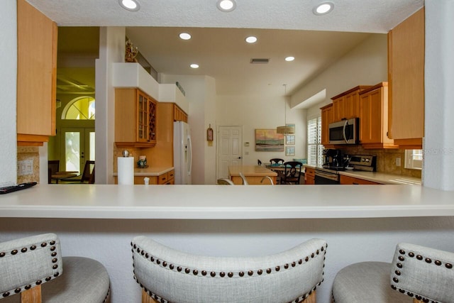 kitchen featuring stainless steel appliances, a kitchen breakfast bar, kitchen peninsula, and decorative backsplash