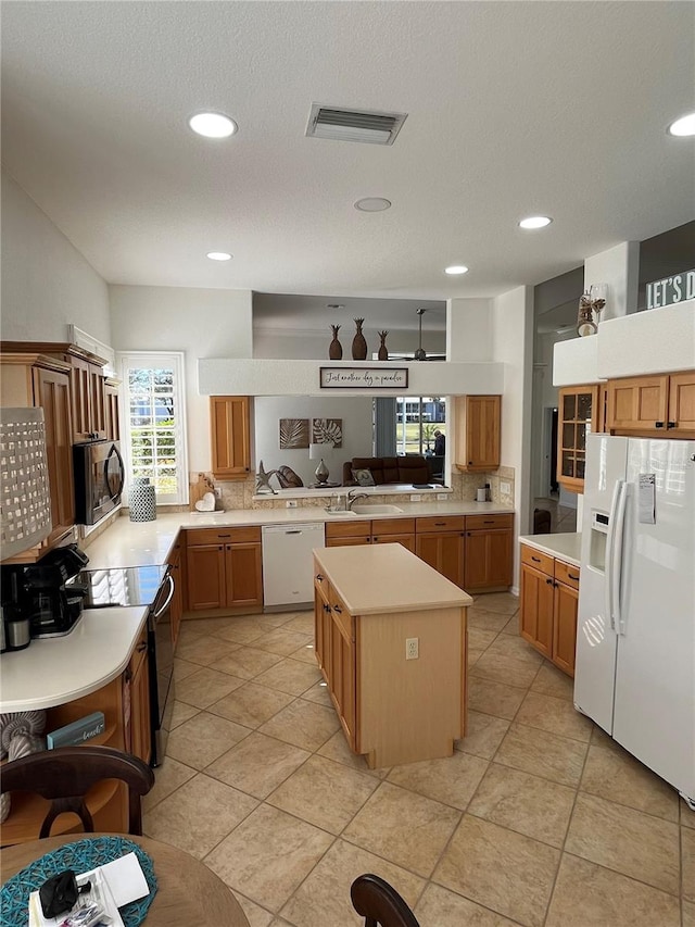 kitchen featuring white appliances, kitchen peninsula, a healthy amount of sunlight, and a kitchen island