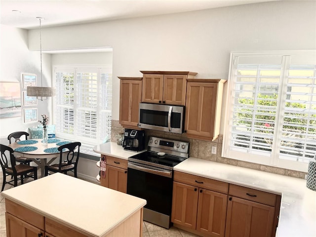 kitchen featuring tasteful backsplash, light tile patterned floors, decorative light fixtures, and appliances with stainless steel finishes