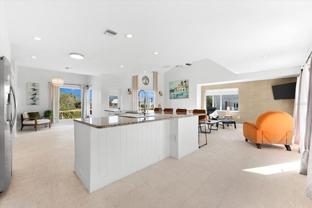 kitchen with a breakfast bar, stainless steel fridge, plenty of natural light, and dark stone countertops