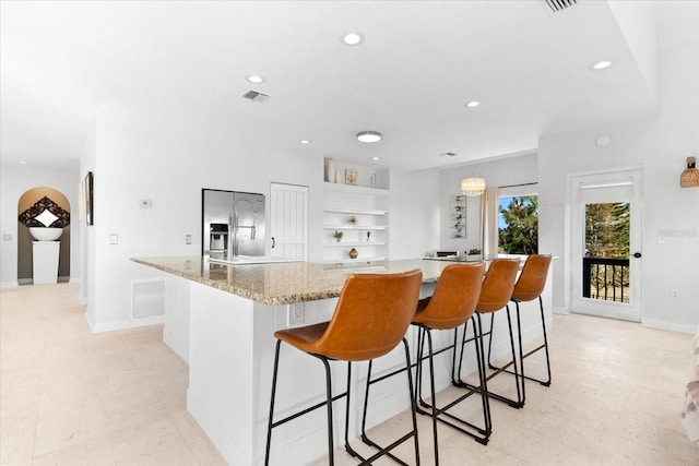 kitchen featuring built in shelves, white cabinetry, light stone counters, a spacious island, and a kitchen bar