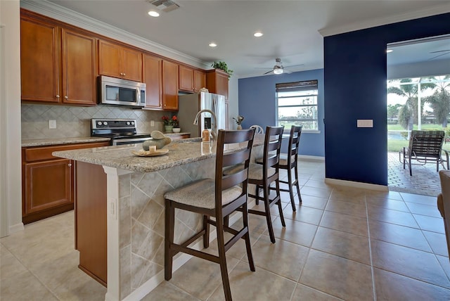 kitchen featuring light stone counters, crown molding, a kitchen bar, a kitchen island with sink, and appliances with stainless steel finishes