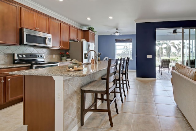 kitchen featuring light stone counters, ornamental molding, stainless steel appliances, a center island with sink, and a breakfast bar area