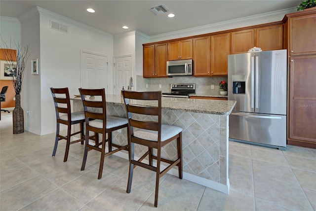 kitchen featuring a kitchen breakfast bar, tasteful backsplash, light stone counters, ornamental molding, and stainless steel appliances