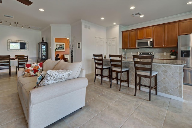 kitchen with rail lighting, a breakfast bar area, light stone countertops, an island with sink, and stainless steel appliances