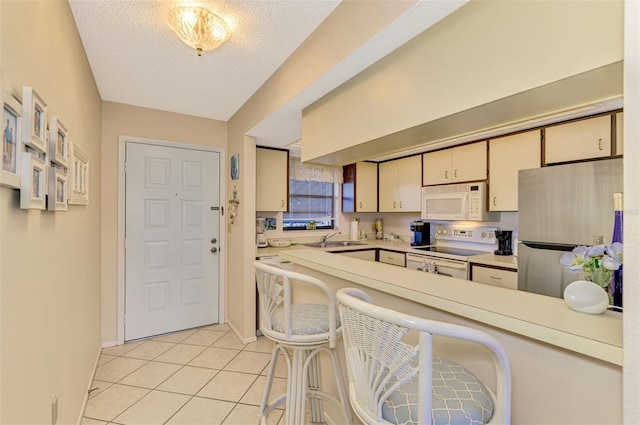 kitchen featuring white appliances, cream cabinets, sink, a textured ceiling, and light tile patterned flooring