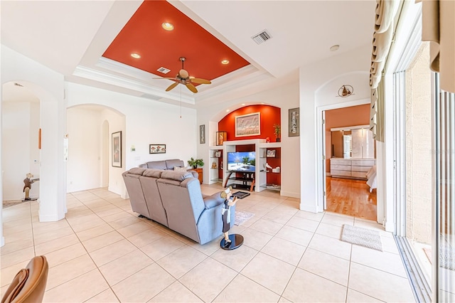 living room featuring light tile patterned floors, crown molding, a raised ceiling, and ceiling fan