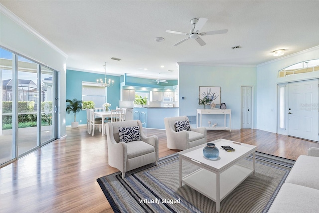 living room with ceiling fan with notable chandelier, ornamental molding, and light hardwood / wood-style floors