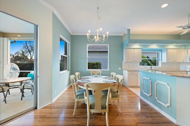 dining space with sink, light wood-type flooring, ornamental molding, and ceiling fan with notable chandelier