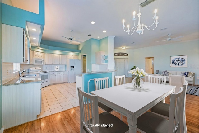 dining space with sink, light hardwood / wood-style flooring, and ceiling fan with notable chandelier