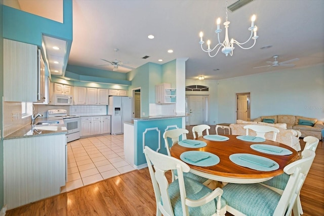 dining area with ceiling fan with notable chandelier, sink, and light hardwood / wood-style flooring