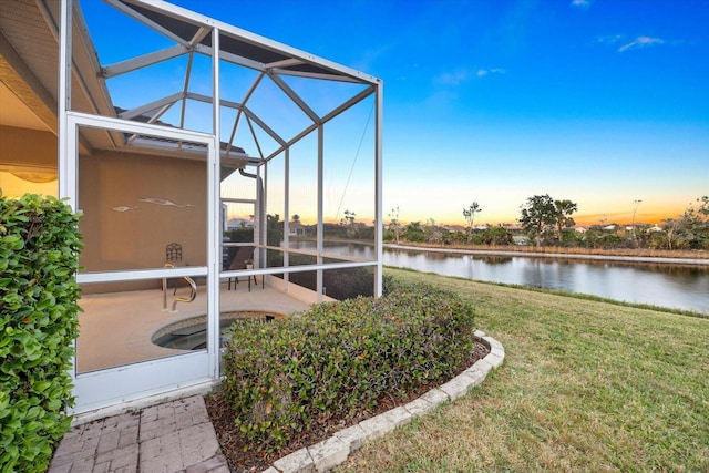 yard at dusk featuring a patio, glass enclosure, and a water view