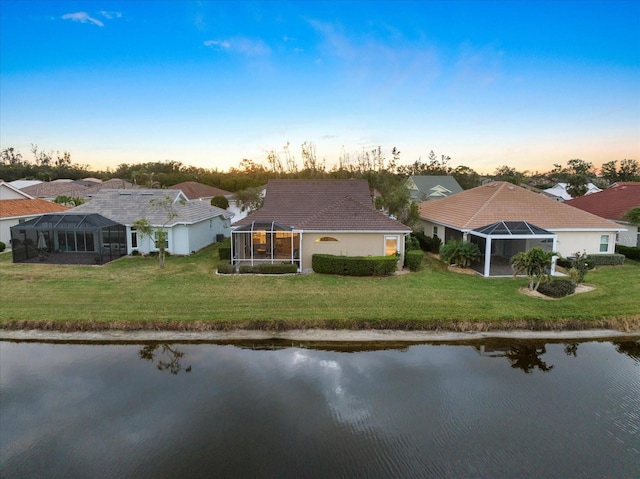 back house at dusk with a yard, glass enclosure, and a water view