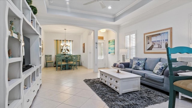 living room featuring a raised ceiling, crown molding, light tile patterned floors, and ceiling fan with notable chandelier