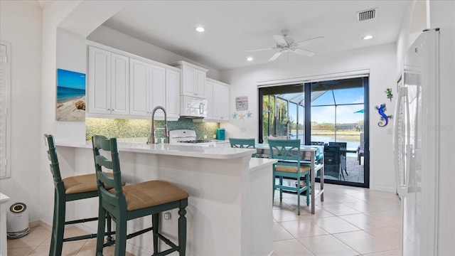 kitchen with white cabinetry, tasteful backsplash, kitchen peninsula, white appliances, and a kitchen bar